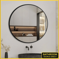 Round black-framed mirror in a bathroom setting with a sink and shelves.