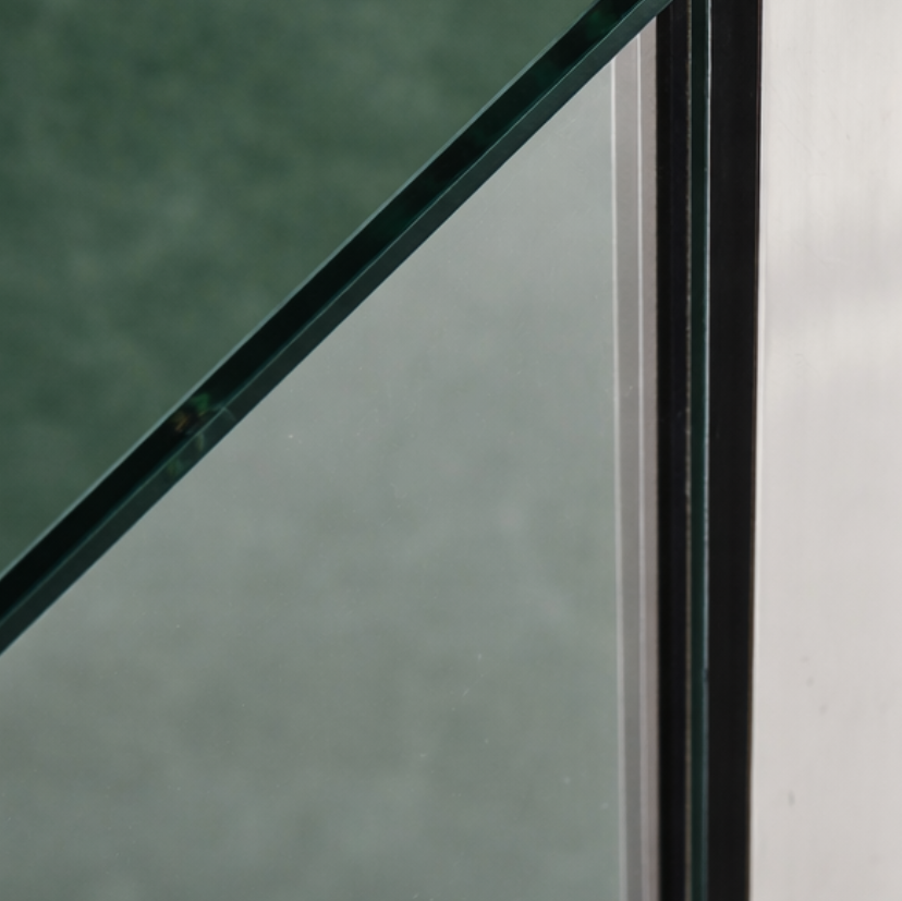Close-up of bath shower screen glass edge with chrome wall profile against green tiled wall