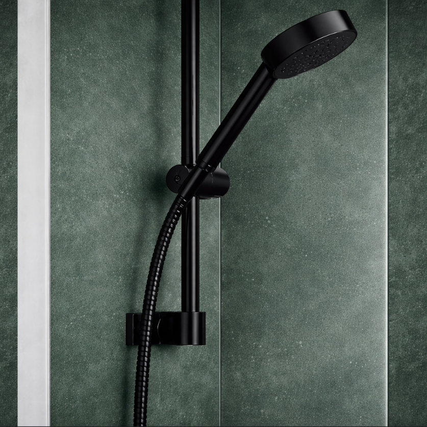 Modern black shower head and rail detail with hose mounted on green tiled bathroom wall behind glass bath screen