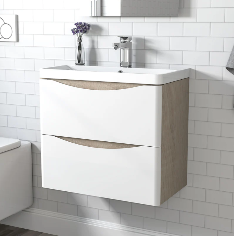Bathroom vanity with white countertop and wooden cabinet against a tiled wall.
