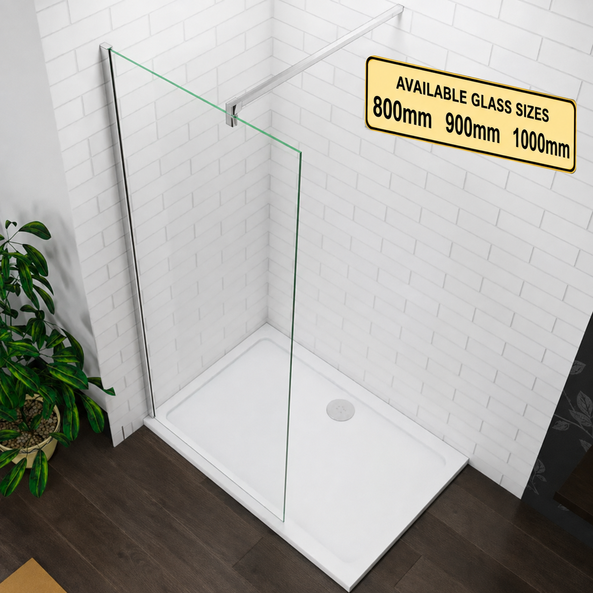 A frameless glass shower screen panel installed in a white tiled bathroom corner with a white shower base and dark wood floor. A yellow sign in the upper right lists available glass sizes 800mm, 900mm, and 1000mm, and a green potted plant is visible on the left.